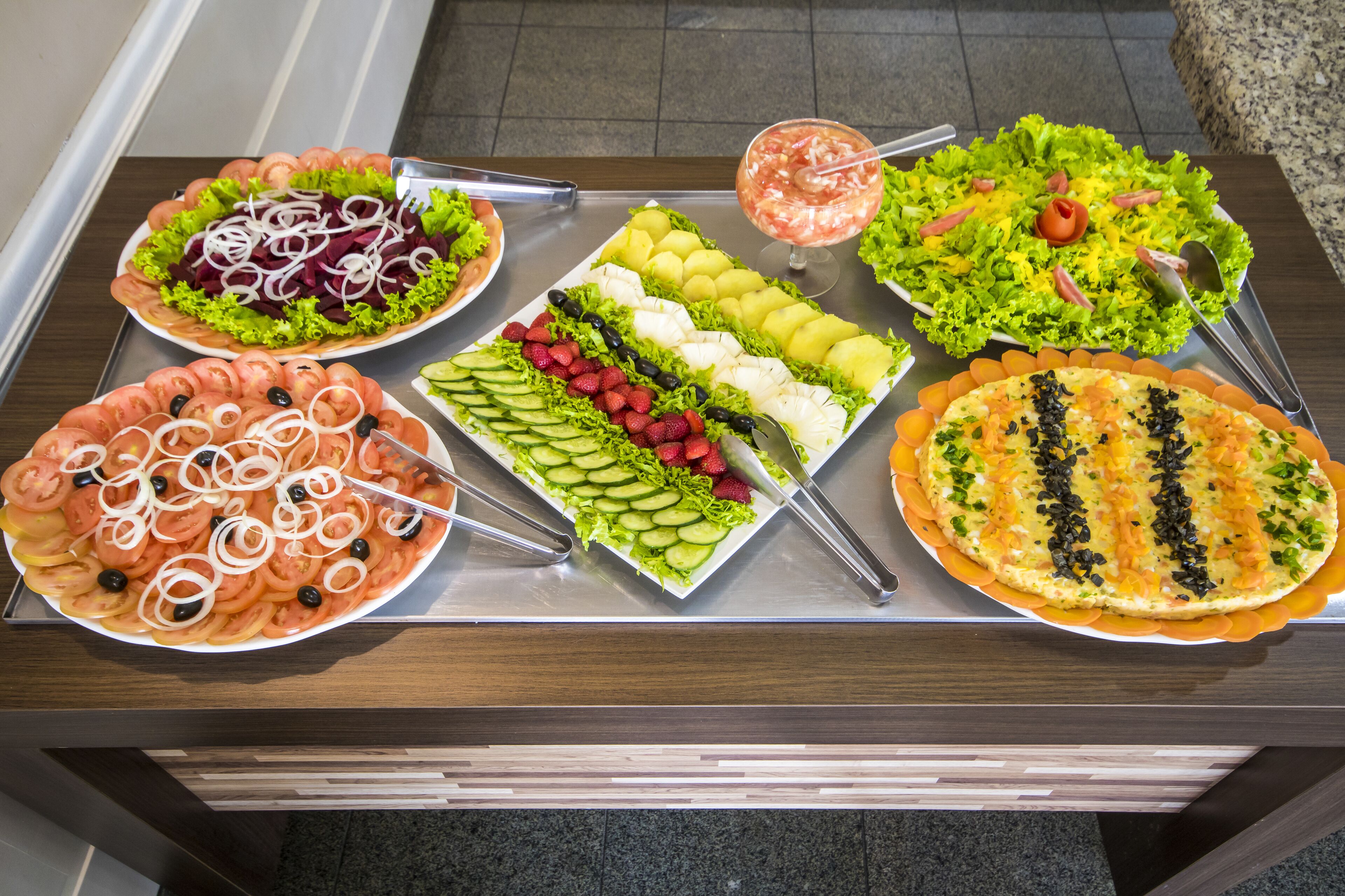A buffet table with various food items including salads, fruits, and a pizza.