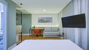 Una habitación de hotel moderna con una cama, un escritorio, un sofá y un televisor montado en la pared.