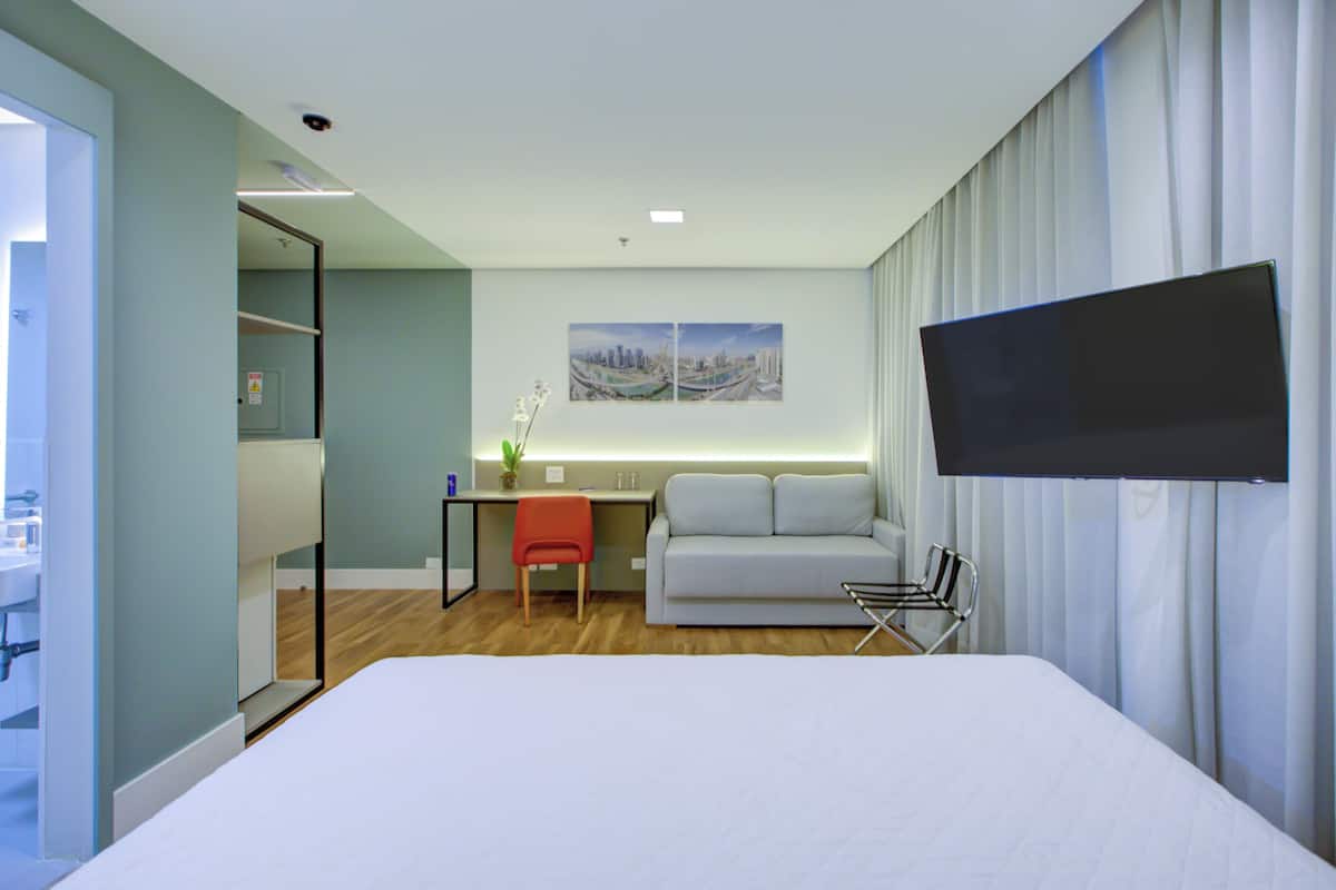Una habitación de hotel moderna con una cama, un escritorio, un sofá y un televisor montado en la pared.