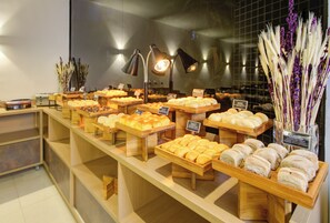 A bakery display with various baked goods and a decorative plant arrangement. - Transamerica Executive Chácara Santo Antônio (São Paulo)