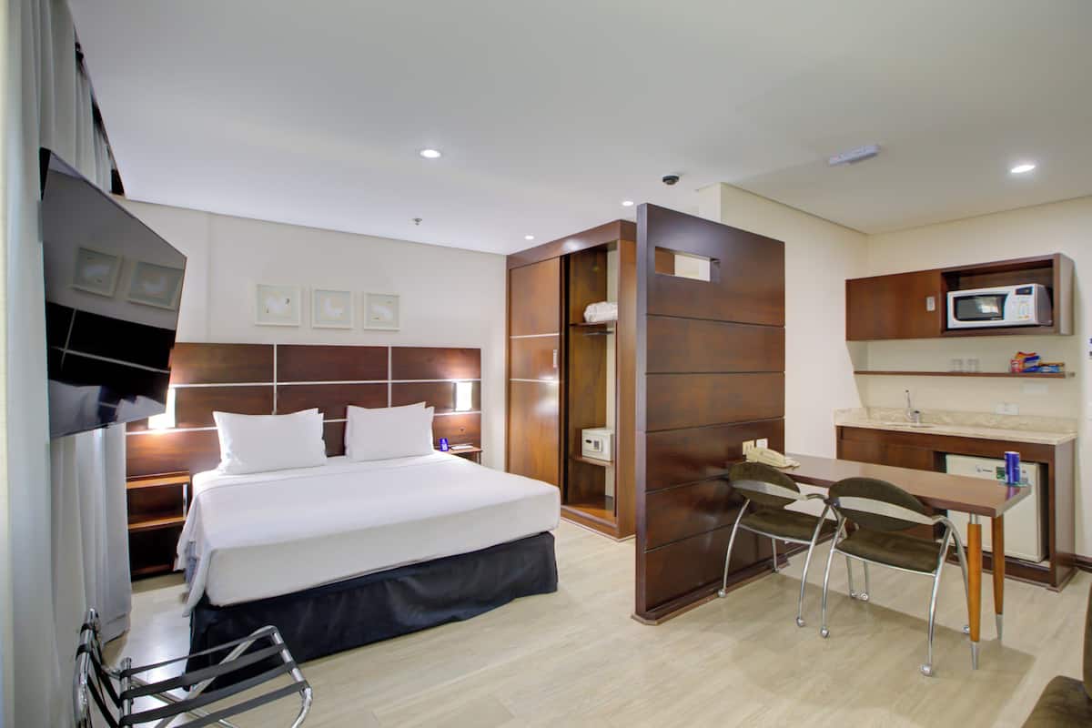 Una habitación de hotel con cama, escritorio, silla, microondas y una pequeña kitchenette.