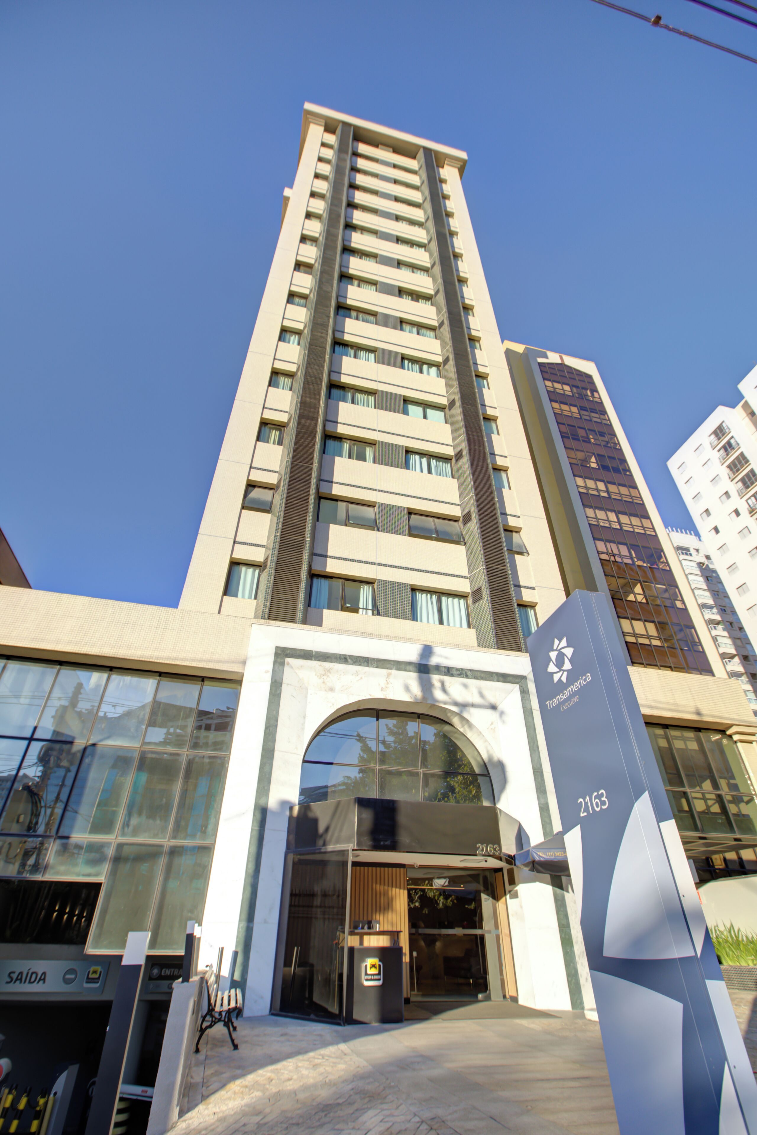 Um edifício alto com design moderno, destacando uma entrada imponente com fachada de vidro e uma placa indicando o endereço.