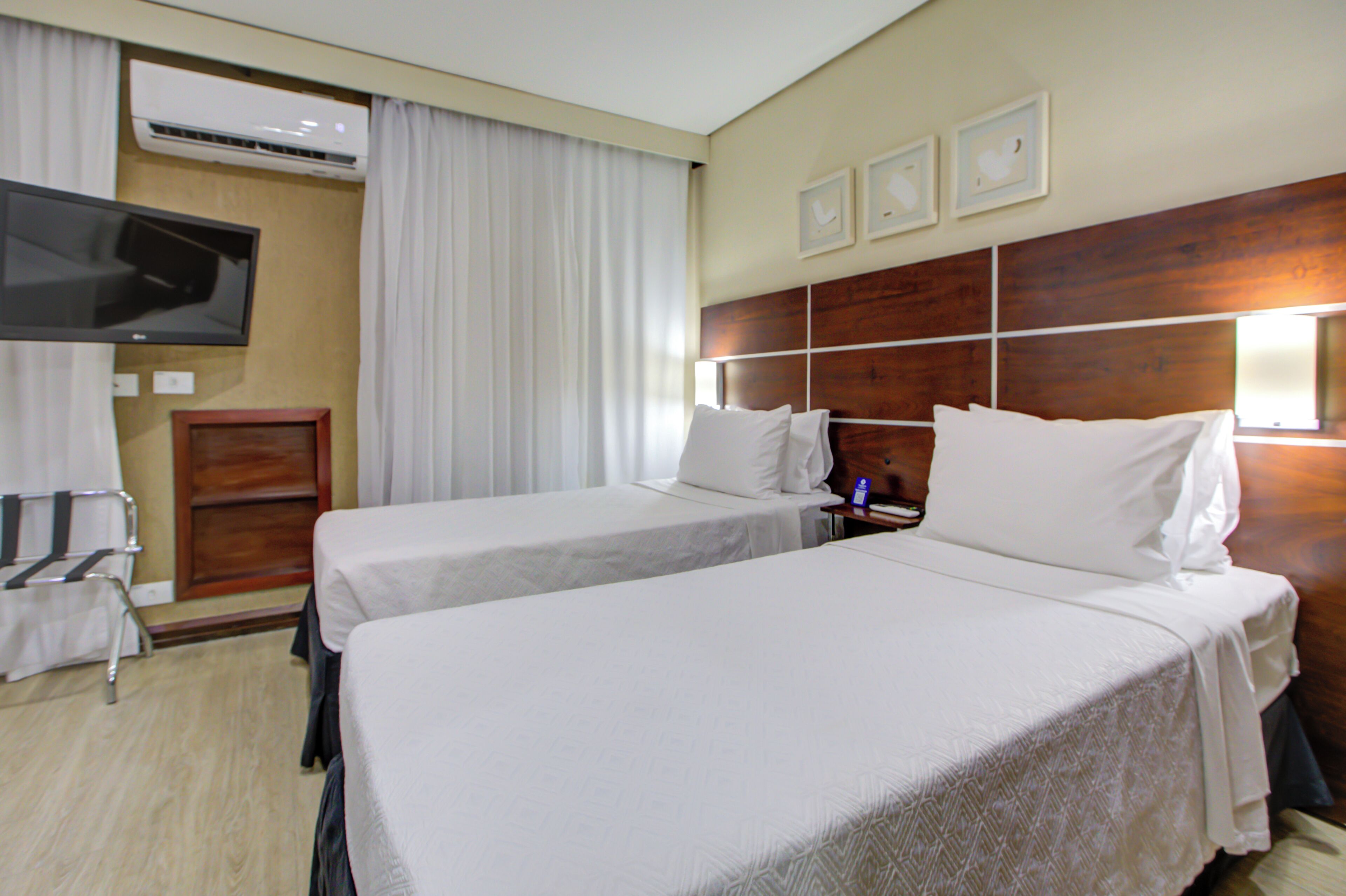 Habitación de hotel con dos camas, un televisor, cabecero de madera y aire acondicionado instalado en la pared.