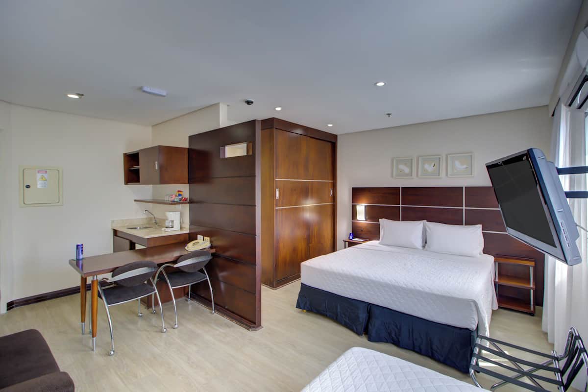 Una habitación de hotel con cama, escritorio, silla y televisor.