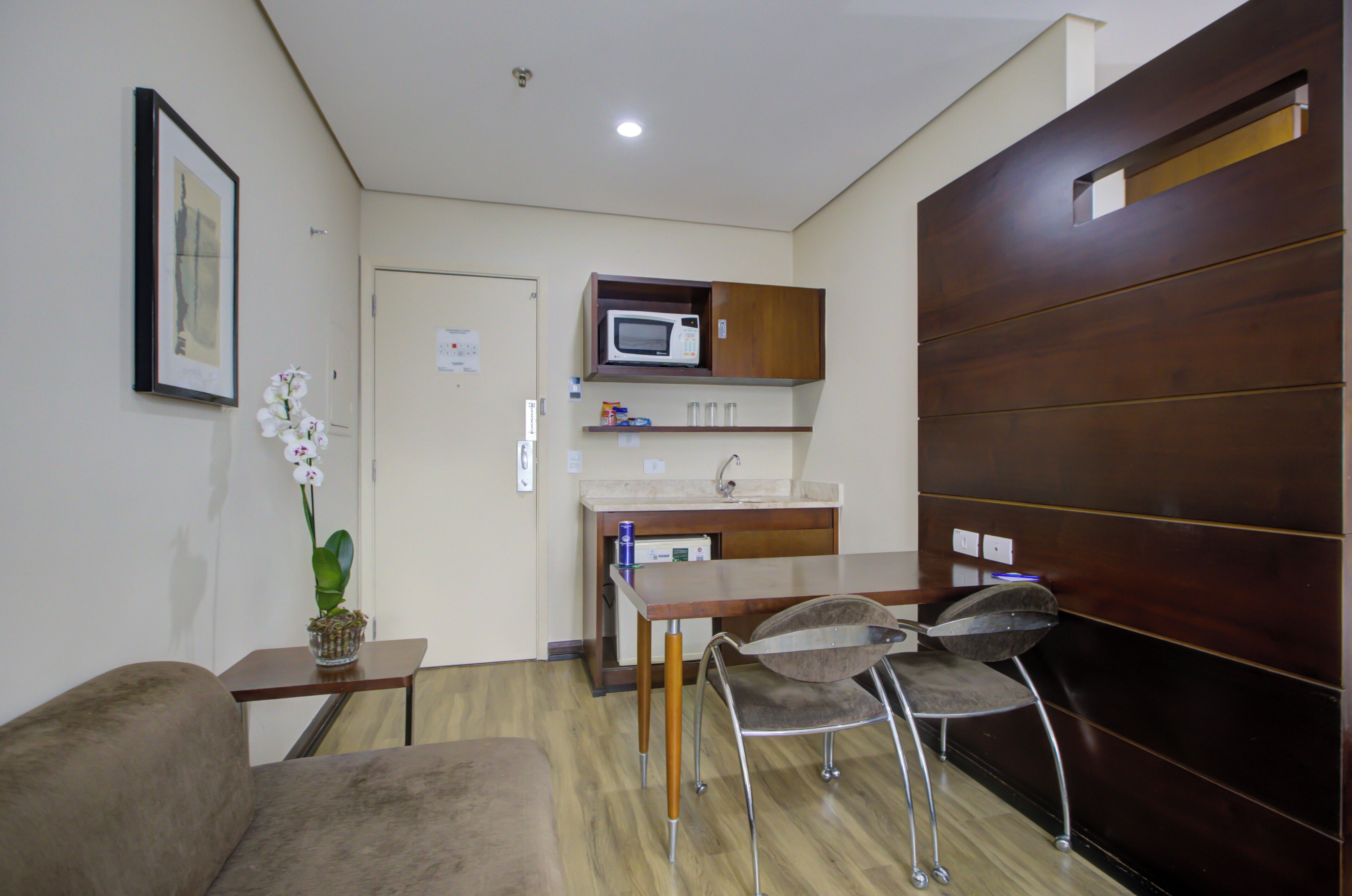 A compact living space with a kitchenette, a dining area with a table and chairs, a sofa, and a potted orchid.