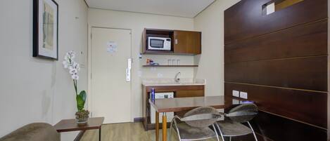 A compact living space with a kitchenette, a dining area with a table and chairs, a sofa, and a potted orchid.