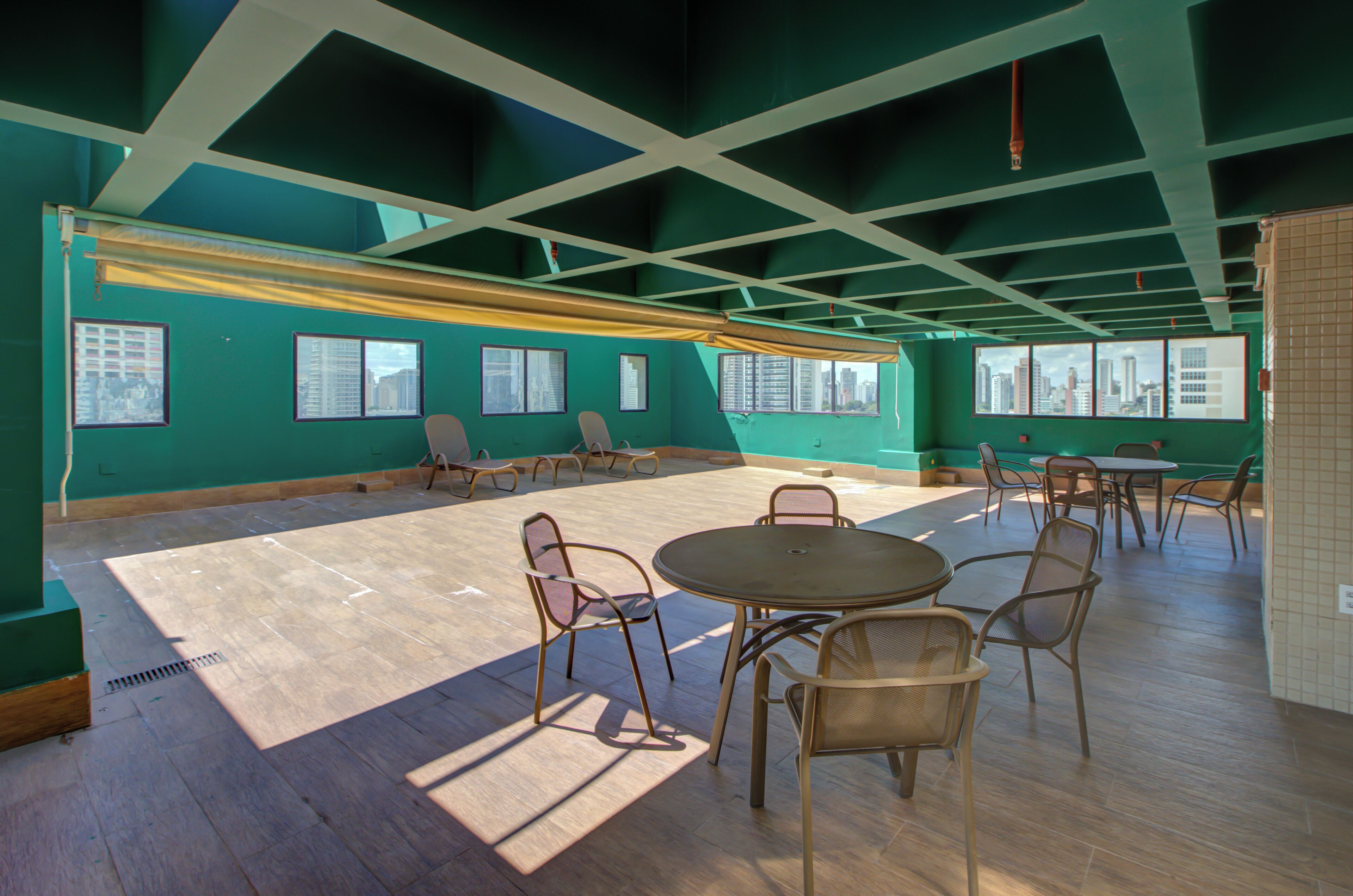 Une pièce spacieuse avec un plafond haut, de grandes fenêtres et un espace salon central comprenant des chaises et une table.