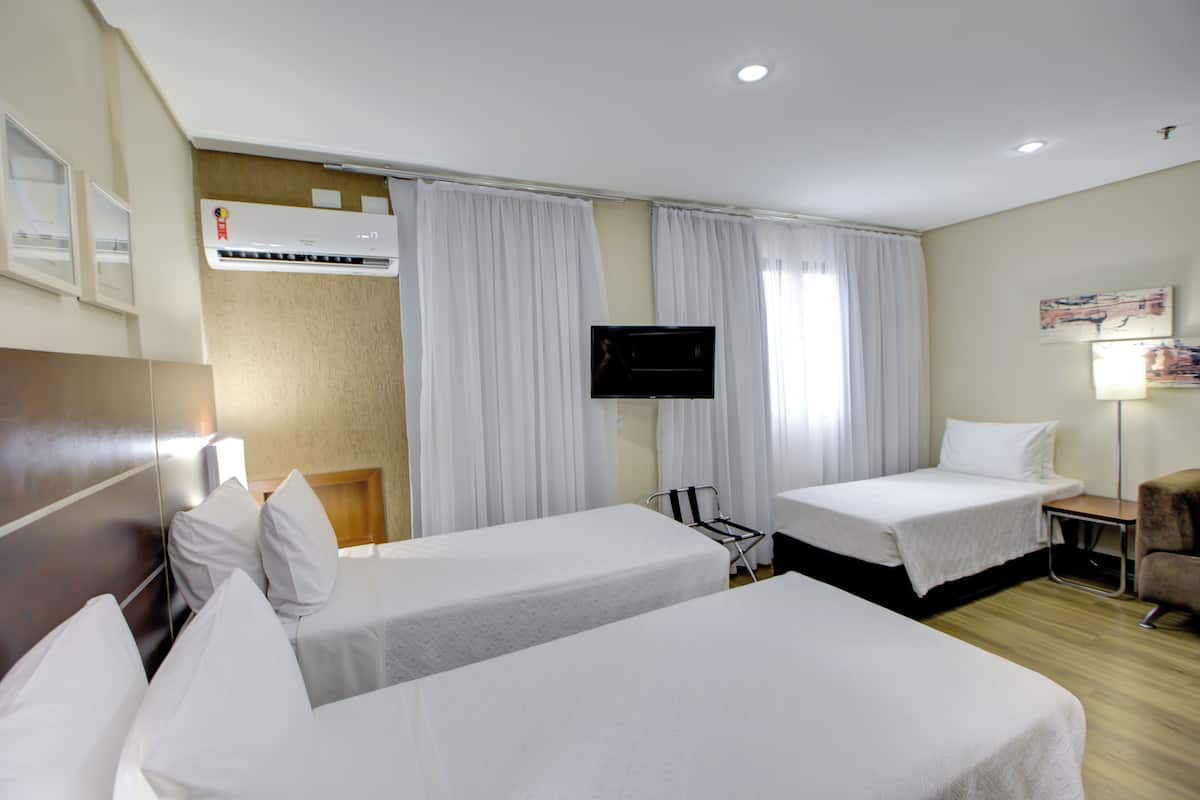 Habitación de hotel con dos camas, televisión de pantalla plana, aire acondicionado y un escritorio con silla.