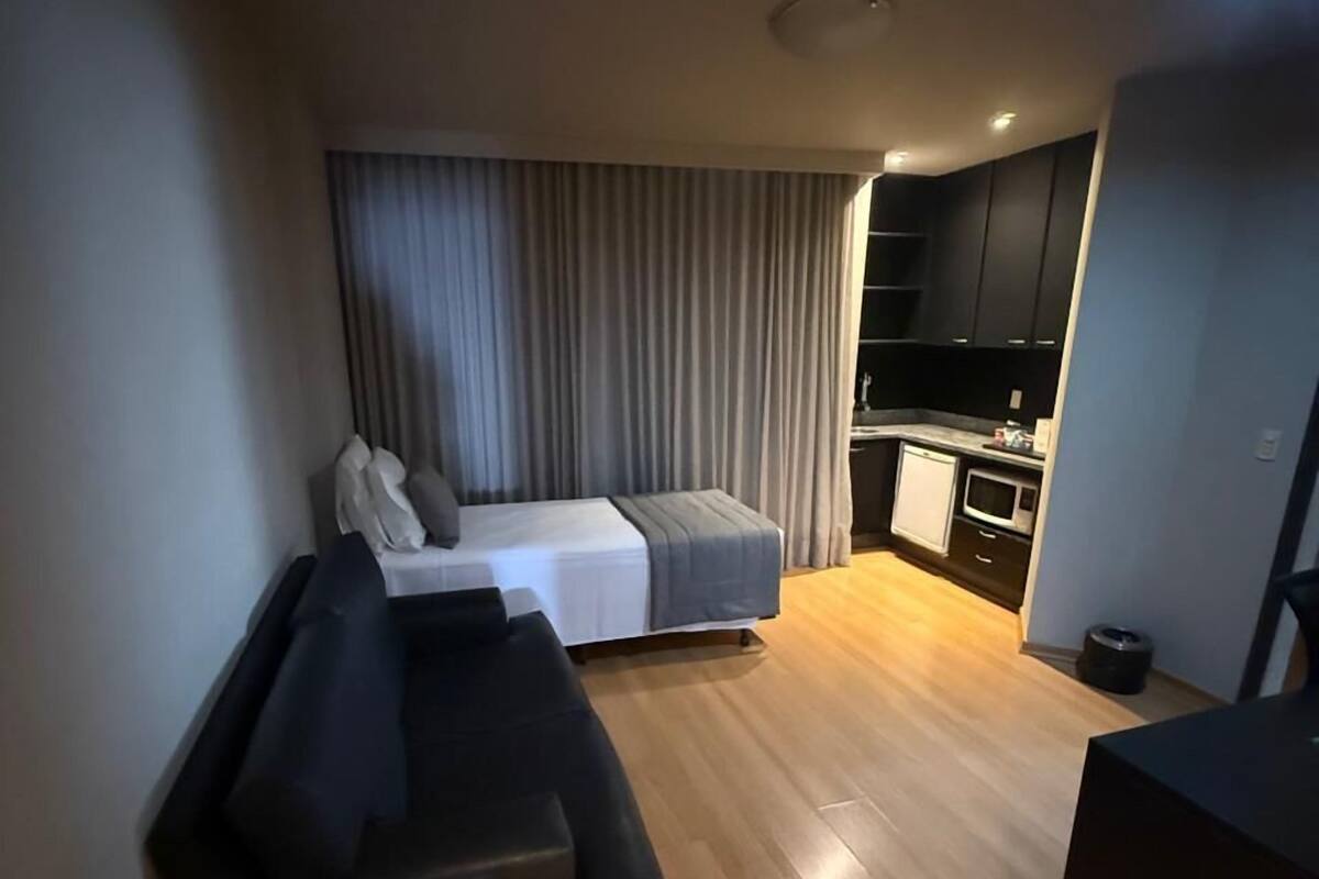 Un espai vital reduït amb un sofà, una taula petita, un llit i una zona de cuina equipada.