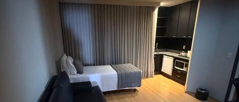 Un espacio habitable compacto con sofá, una mesita, cama y una zona de kitchenette.