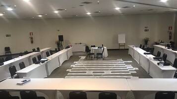 Een vergaderzaal met lange tafels, stoelen, een whiteboard en een spreekgestalte.