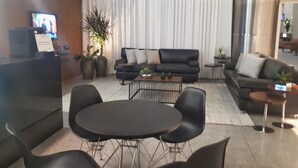 A modern hotel lobby with a reception desk, black leather sofas, a round table, and potted plants. - San Diego Suites Lourdes (Belo Horizonte)