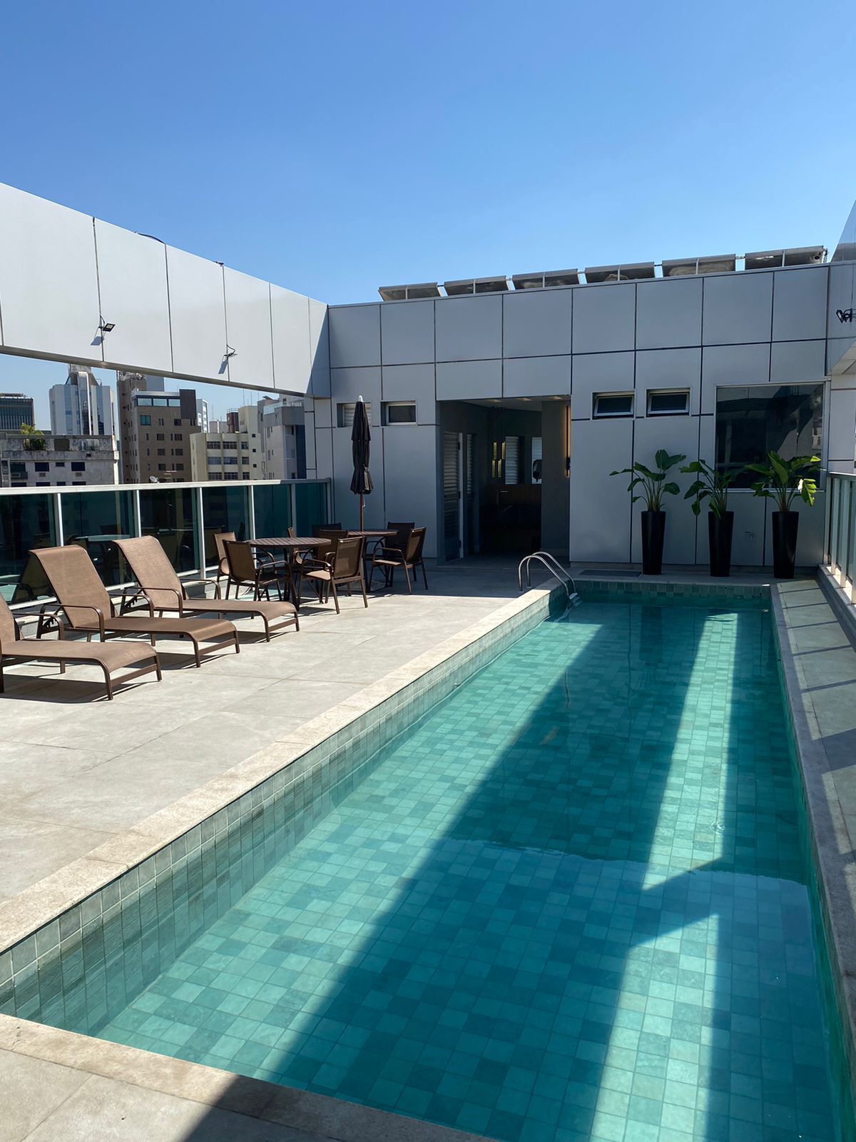 A rooftop pool area with lounge chairs and a table, surrounded by a modern building with large windows.