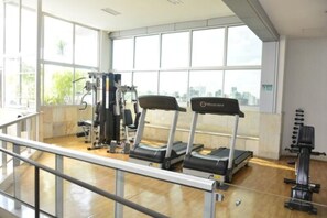 Un gimnasio con cintas de correr, máquinas de pesas y vistas a la ciudad a través de amplios ventanales.