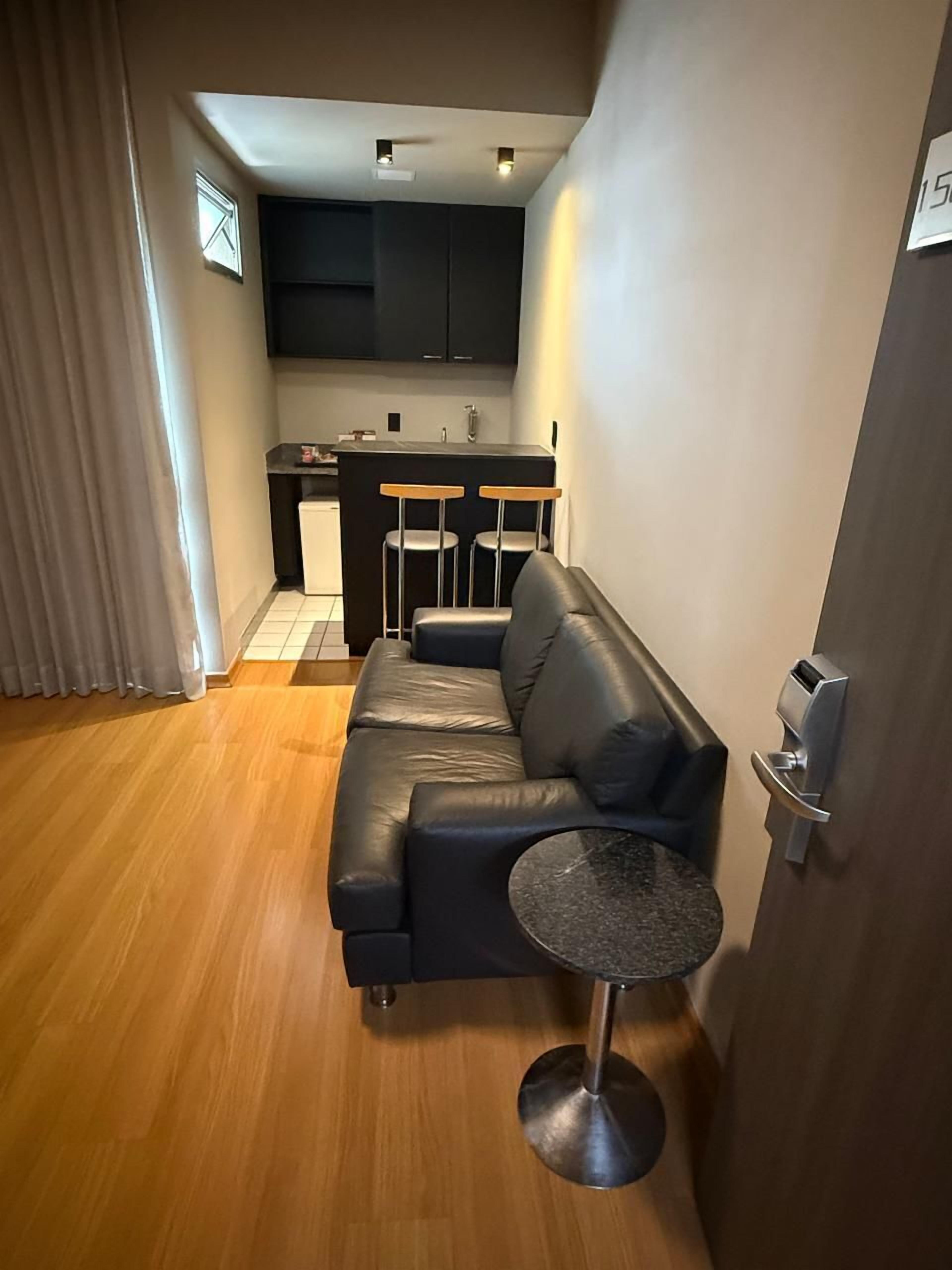 Una sala de estar moderna con un sofá de cuero negro, una mesita redonda y una cocina con un taburete de bar.