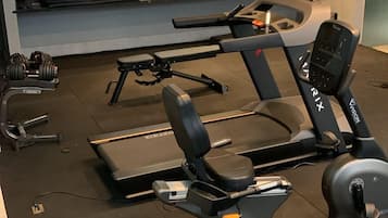 A gym with cardio machines, weightlifting equipment, and a bench.