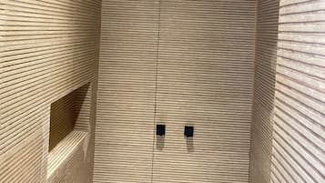 Un baño moderno con un diseño de pared de listones de madera, ducha empotrada en el techo y un pequeño estante con artículos de tocador.