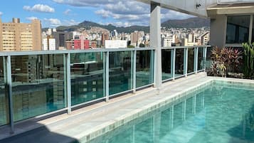 A rooftop pool with a city view, glass railings, and a clear sky.
