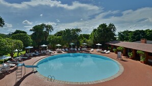 A circular pool with lounge chairs and umbrellas, surrounded by palm trees and a clear sky. - Hotel Deville Express Guaíra (Guaira)