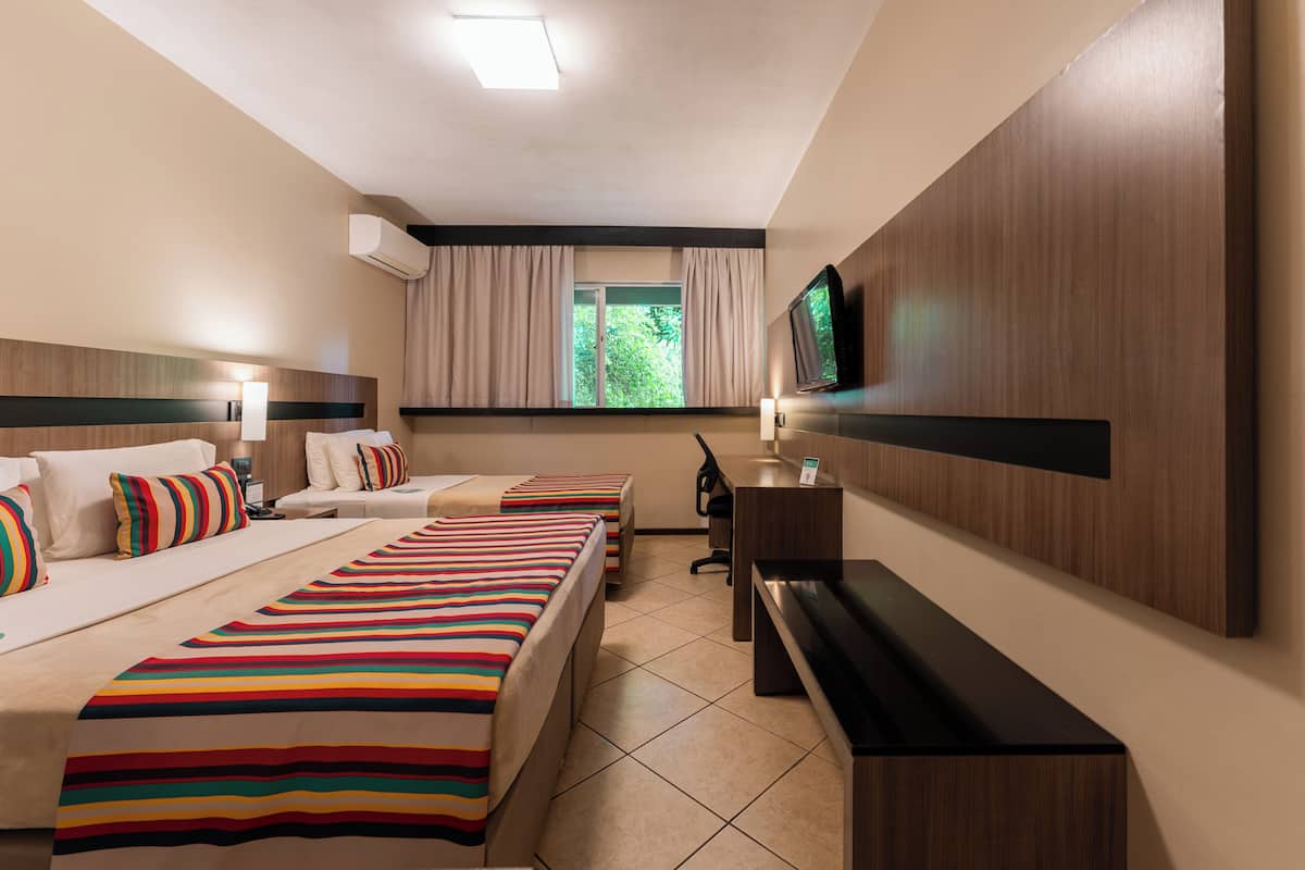 Habitación de hotel con dos camas, un escritorio, un televisor y una ventana con cortinas.