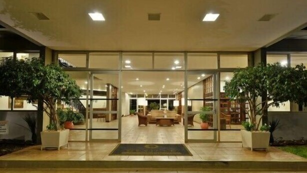 A hotel entrance with a glass door, indoor plants, a reception desk, and a seating area with tables and chairs. - Hotel Deville Express Guaíra (Guaira)