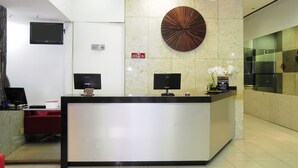 A reception area with a modern design, featuring a reception desk, two monitors, a decorative wall piece, and a small plant. - Bristol Merit Hotel (Belo Horizonte)