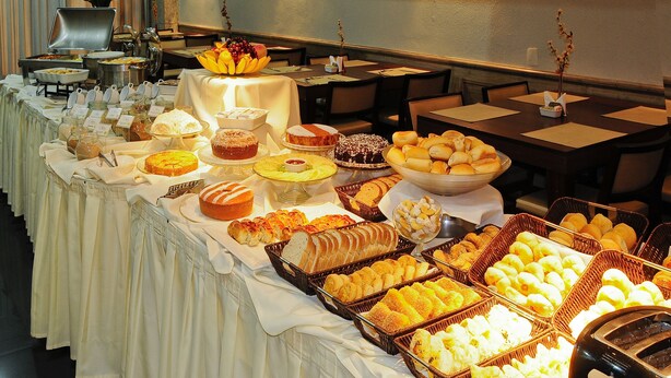 A buffet with various food items and a vase of flowers. - Bristol Merit Hotel (Belo Horizonte)