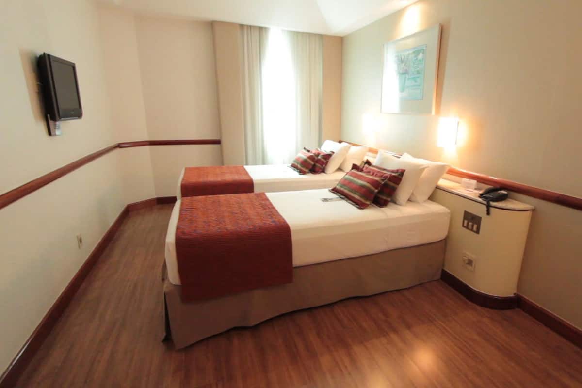Una habitación de hotel con dos camas, una mesita de noche, un teléfono y un televisor instalado en la pared.