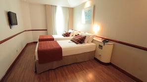 Ein Hotelzimmer mit zwei Betten, einem Nachttisch, einem Telefon und einem am Wand montierten Fernseher.