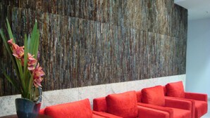 A modern lobby with a textured wall, a row of red upholstered sofas, and a vase with pink flowers on a wooden table. - Bristol Merit Hotel (Belo Horizonte)