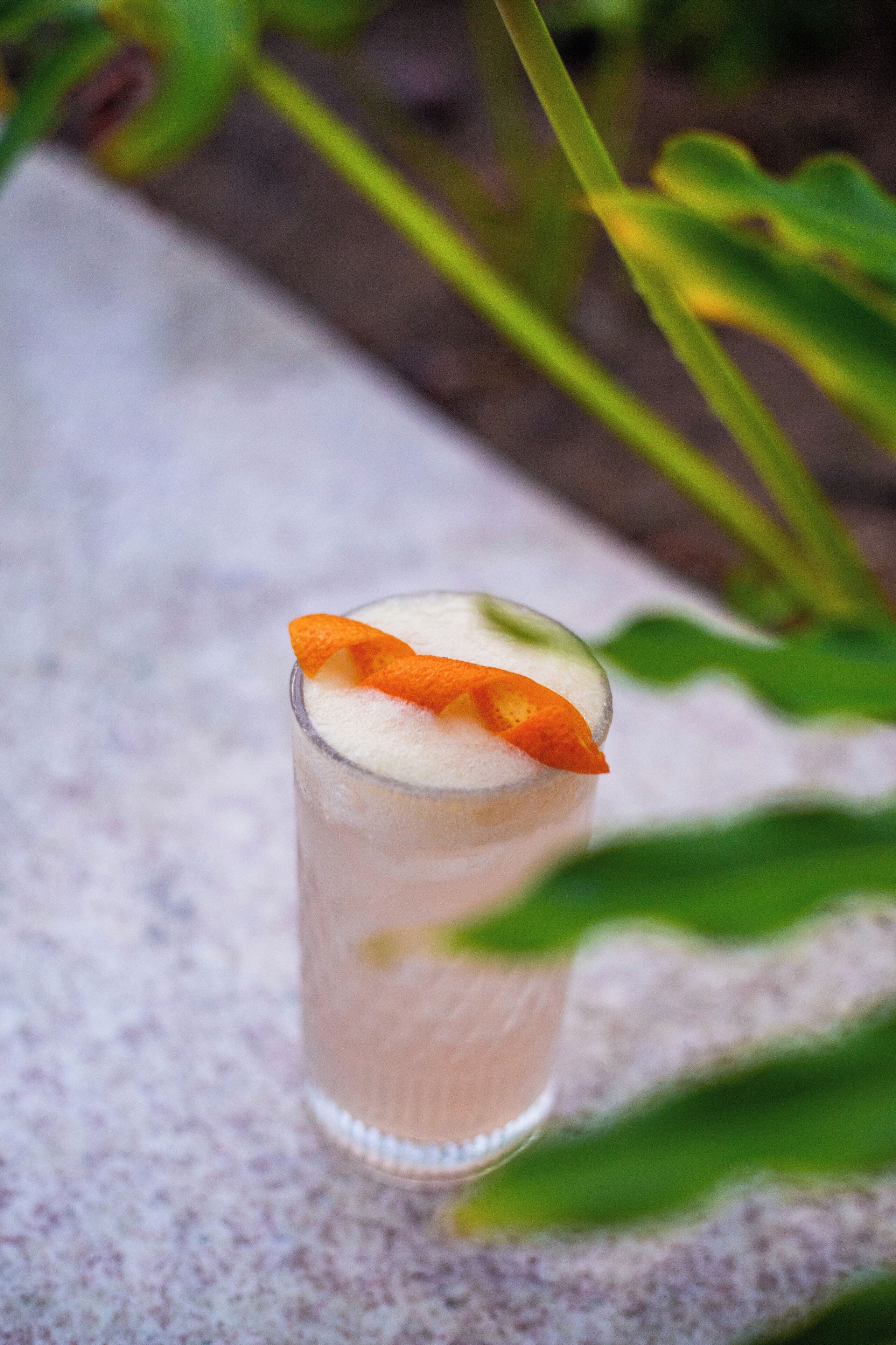 A glass of a beverage with a garnish on a textured surface.