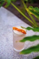 A glass of a beverage with a garnish on a textured surface.