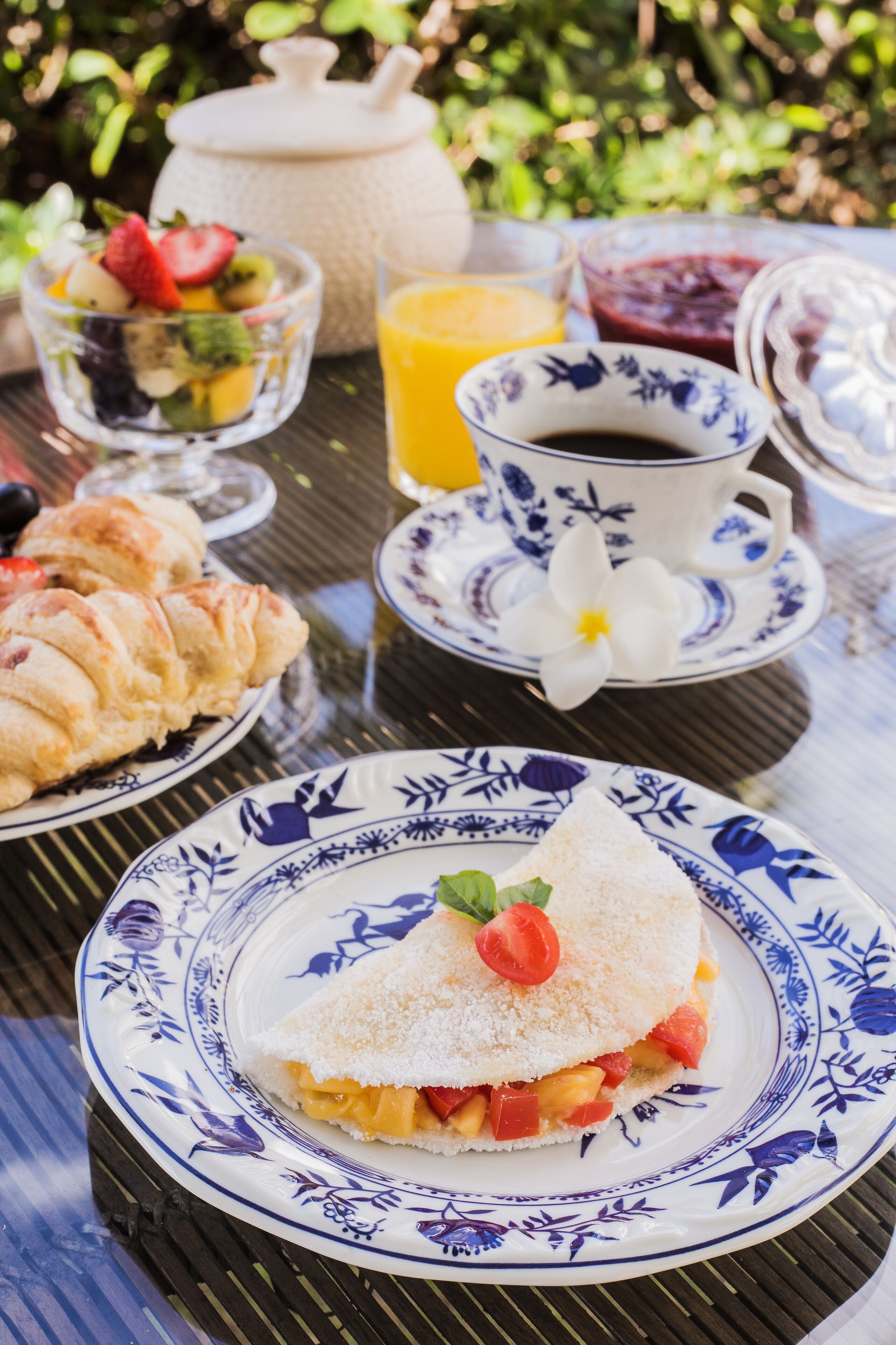 A table with a crepe, a glass of orange juice, a cup of coffee, and a bowl of fruit salad.