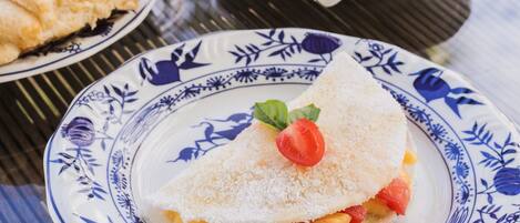 A table with a crepe, a glass of orange juice, a cup of coffee, and a bowl of fruit salad.