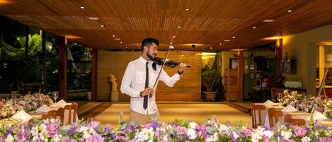 A man playing a violin at a wedding reception with tables set for guests and floral centerpieces.