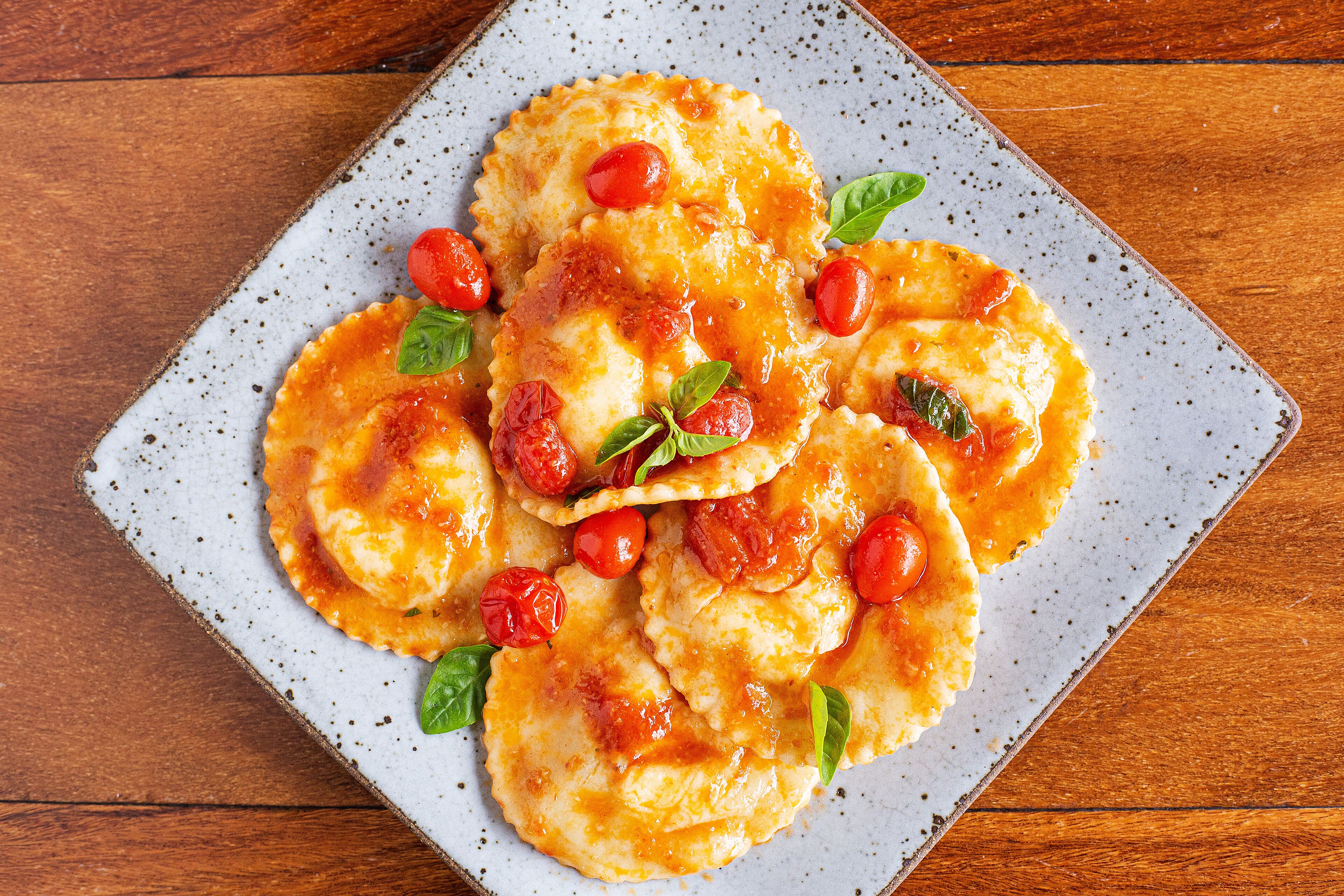 Une assiette de raviolis aux tomates cerises et aux feuilles de basilic.