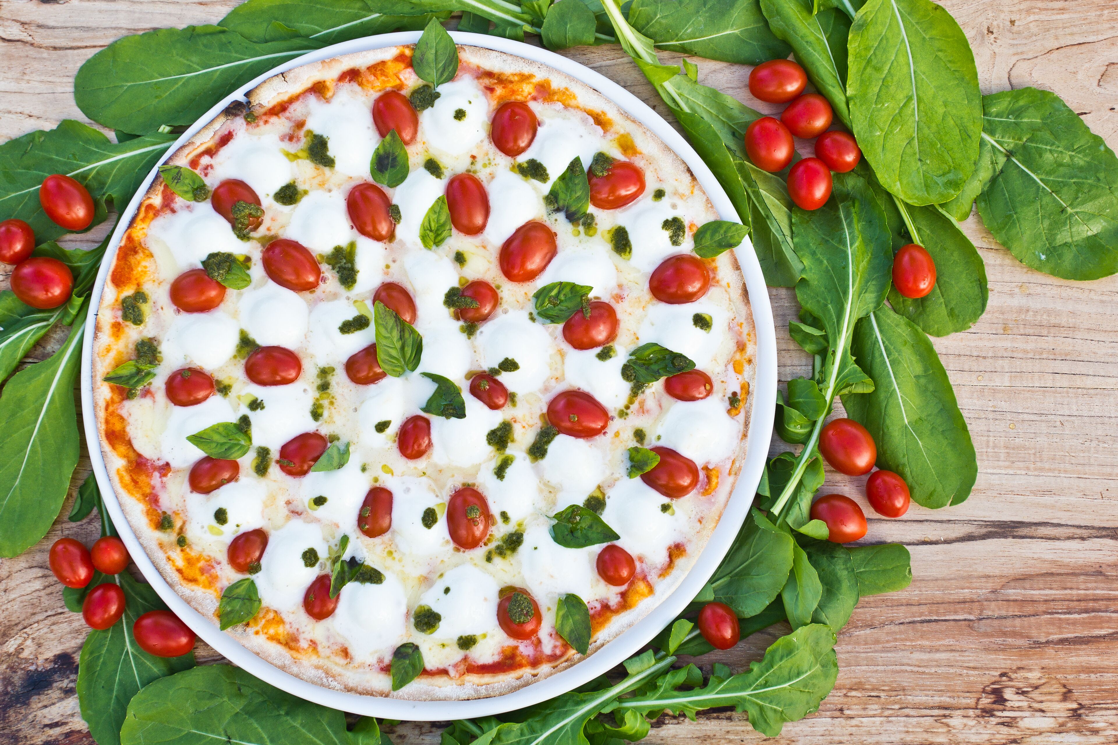 A pizza with tomatoes and basil leaves on a wooden table.