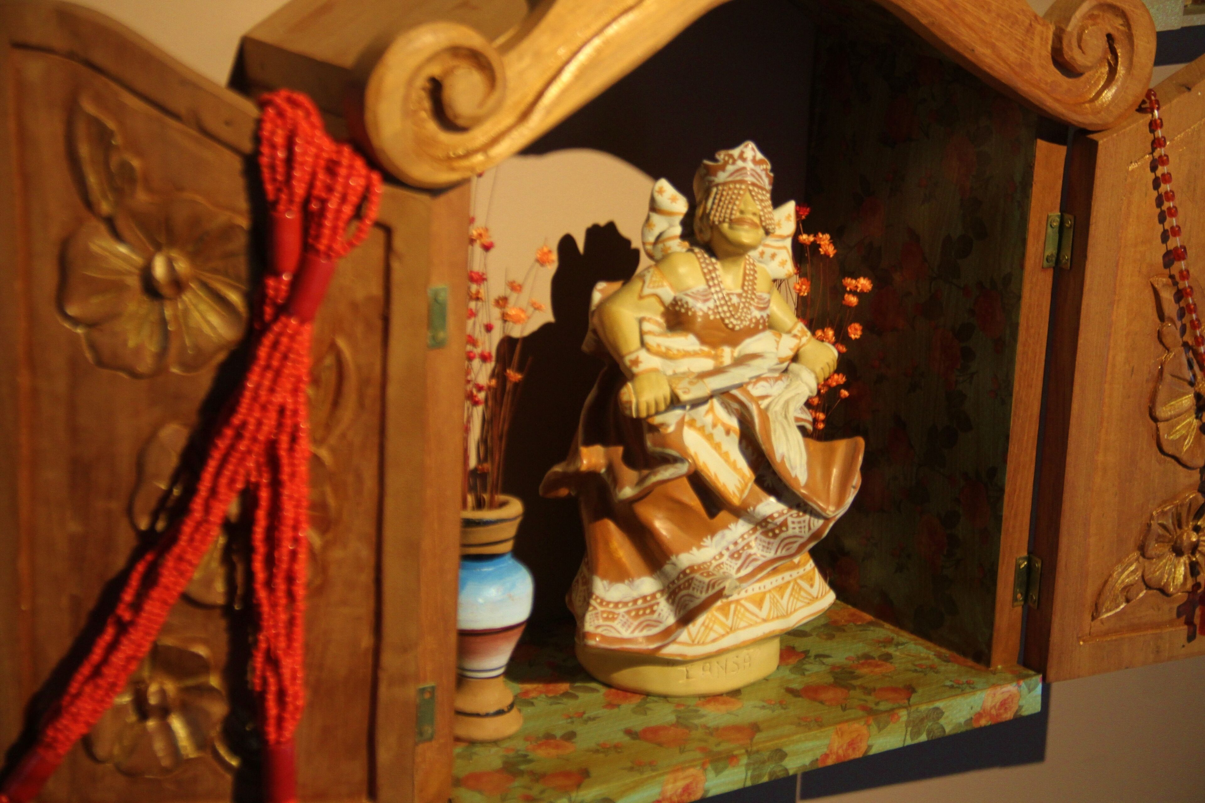 Un mueble de madera con una figura decorativa, un cordón de cuentas rojas y un estante con estampado floral.