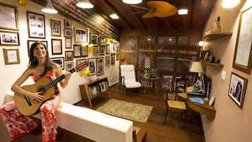 Ein Zimmer mit Holzbalkendecke, einem weißen Sofa, einer Gitarre und einer Wand mit gerahmten Fotos und einem Bücherregal.