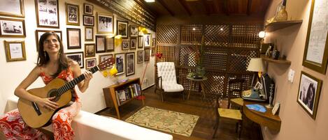 Una habitación con techo de madera, un sofá blanco, una guitarra y una pared decorada con fotografías enmarcadas y una estantería.