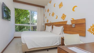 A hotel room with a bed, a desk, and a window with a view of greenery.