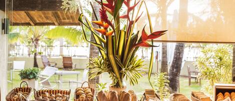 A buffet table with various breads and pastries, a vase with red flowers, and a view of a garden through a window.