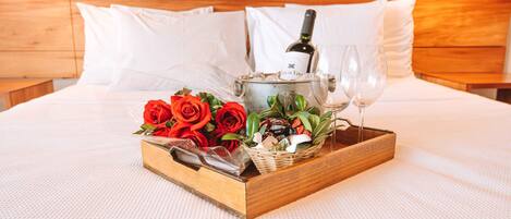 A bed with a wooden headboard, a tray with a bottle of wine, glasses, and a basket of red roses.