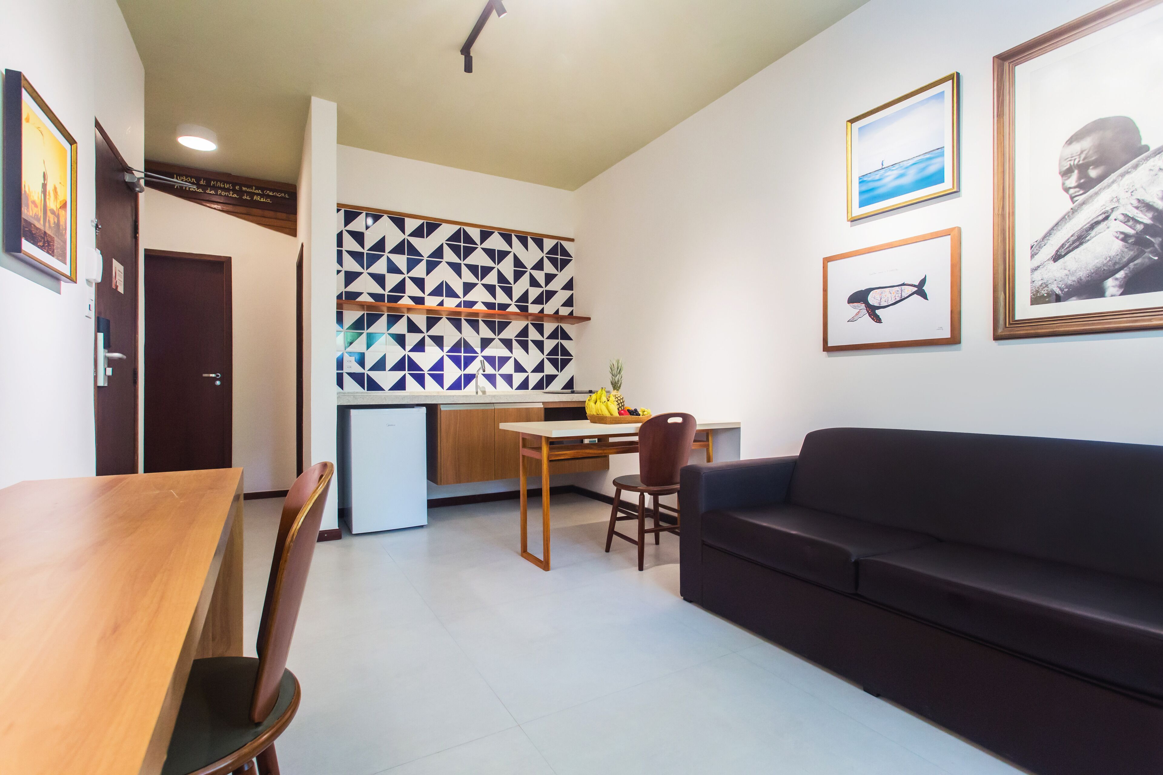 A modern living room with a wooden dining table, a dark sofa, and a kitchen area with a geometric backsplash.