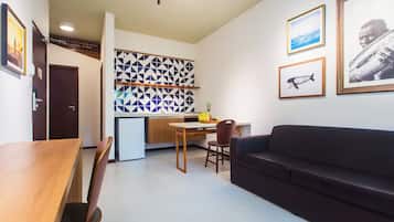 Una sala de estar moderna con una mesa de comedor de madera, un sofá oscuro y una cocina con salpicadero geométrico.
