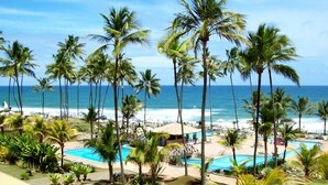 Un resort con varias piscinas, palmeras y vista al mar.