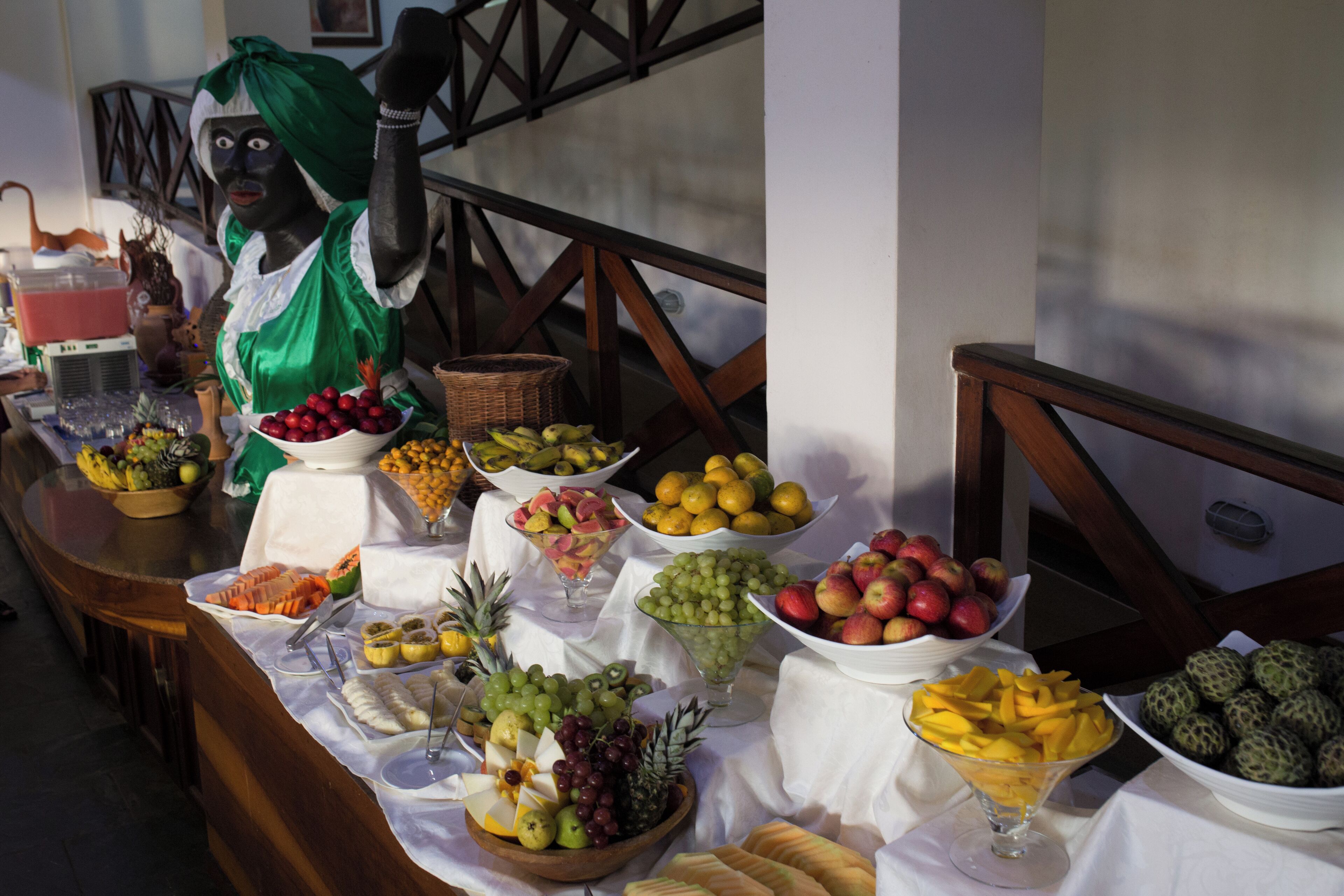 A buffet table with various fruits and snacks, a wicker basket, and a decorative figure.