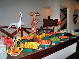 Un bufé con diversas frutas y una estatua decorativa de una mujer sosteniendo una cesta.