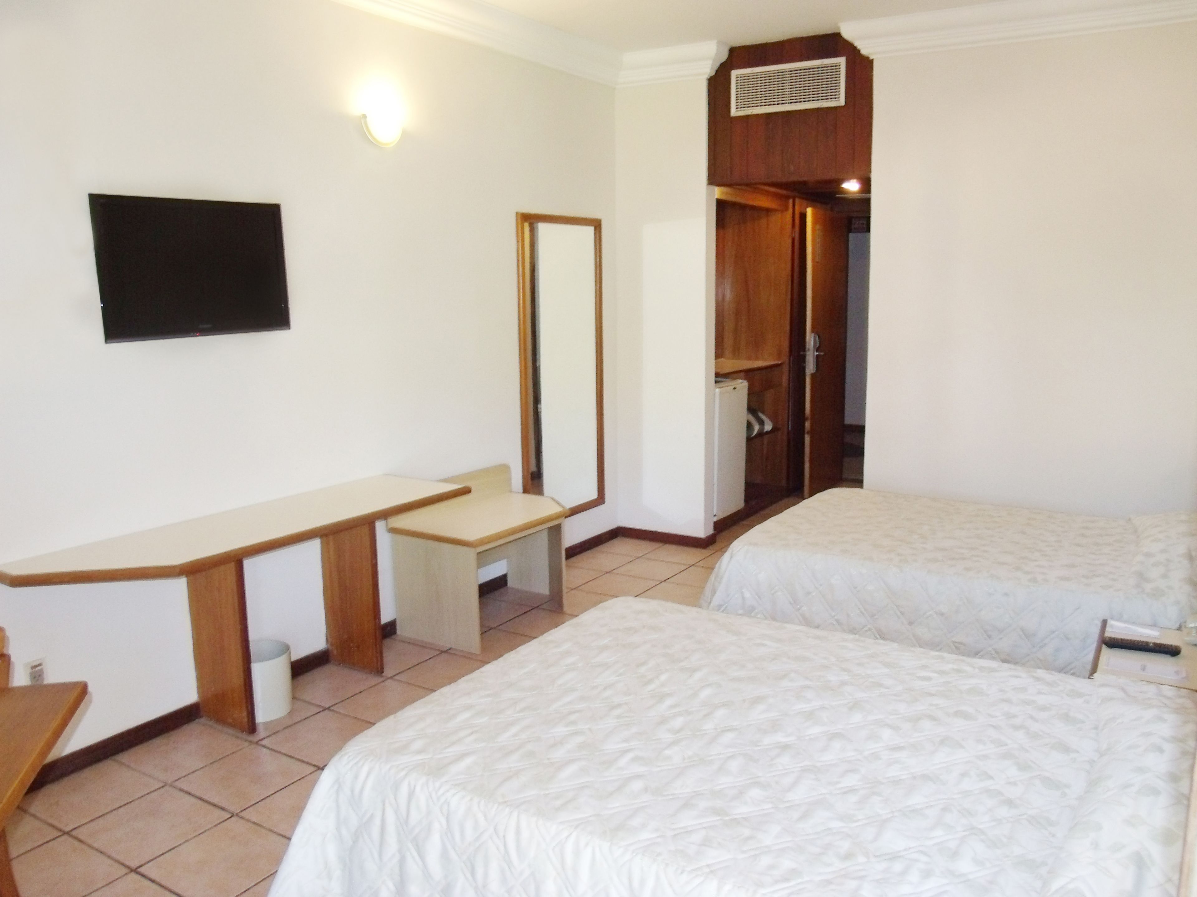 A hotel room with two beds, a desk, a chair, a TV, and a wardrobe.