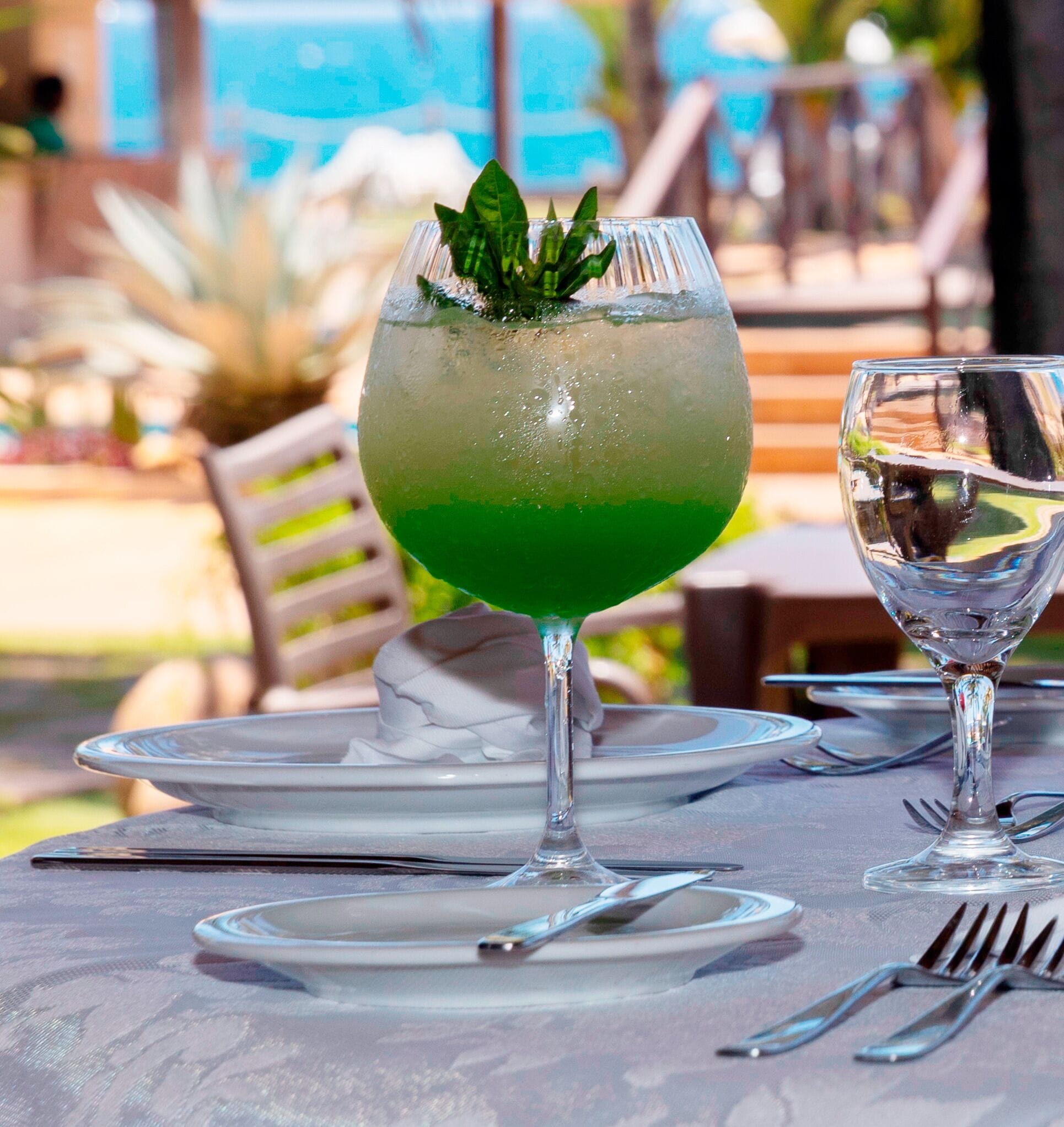 A table set with a glass of green cocktail garnished with mint, a clear glass of water, and a plate with cutlery.